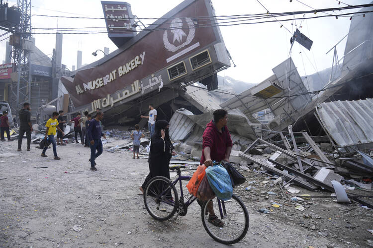 Palestinians walk by the destroyed building of Al Nuseirat Bakery in an Israeli airstrike Nusseirat refugee camp Gaza Strip, Wednesday, Oct. 18, 2023. (AP Photo/Hatem Moussa)