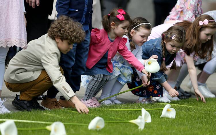 Children place Easter lilies on a lawn during an event in Dublin on March 15, 2020. (CNS photo/Brian Lawless, Reuters)