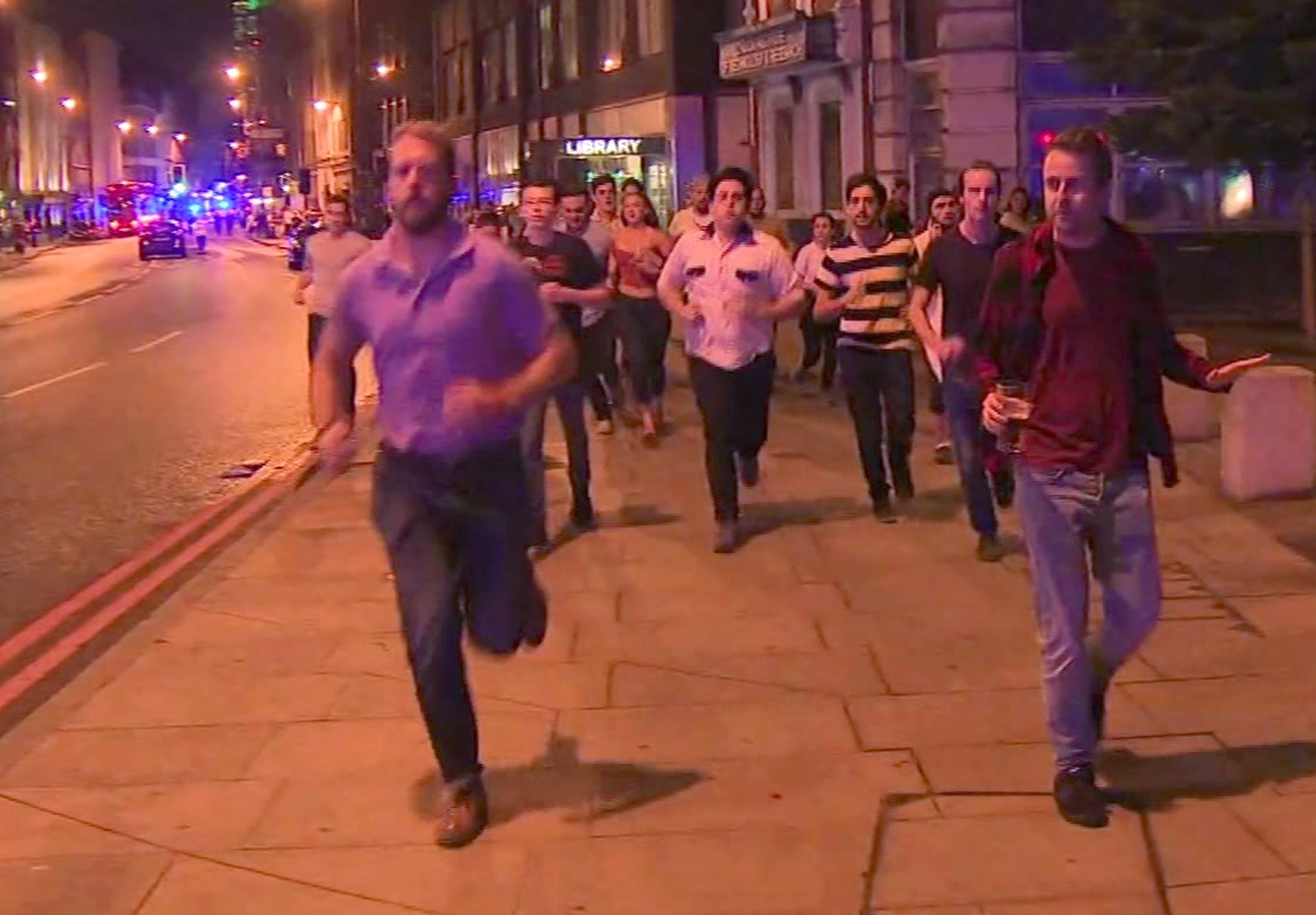 In this image taken from video footage, people run from the scene of attack, alongside a man strolling holding a pint of beer in London on June 3. (Sky news via AP)
