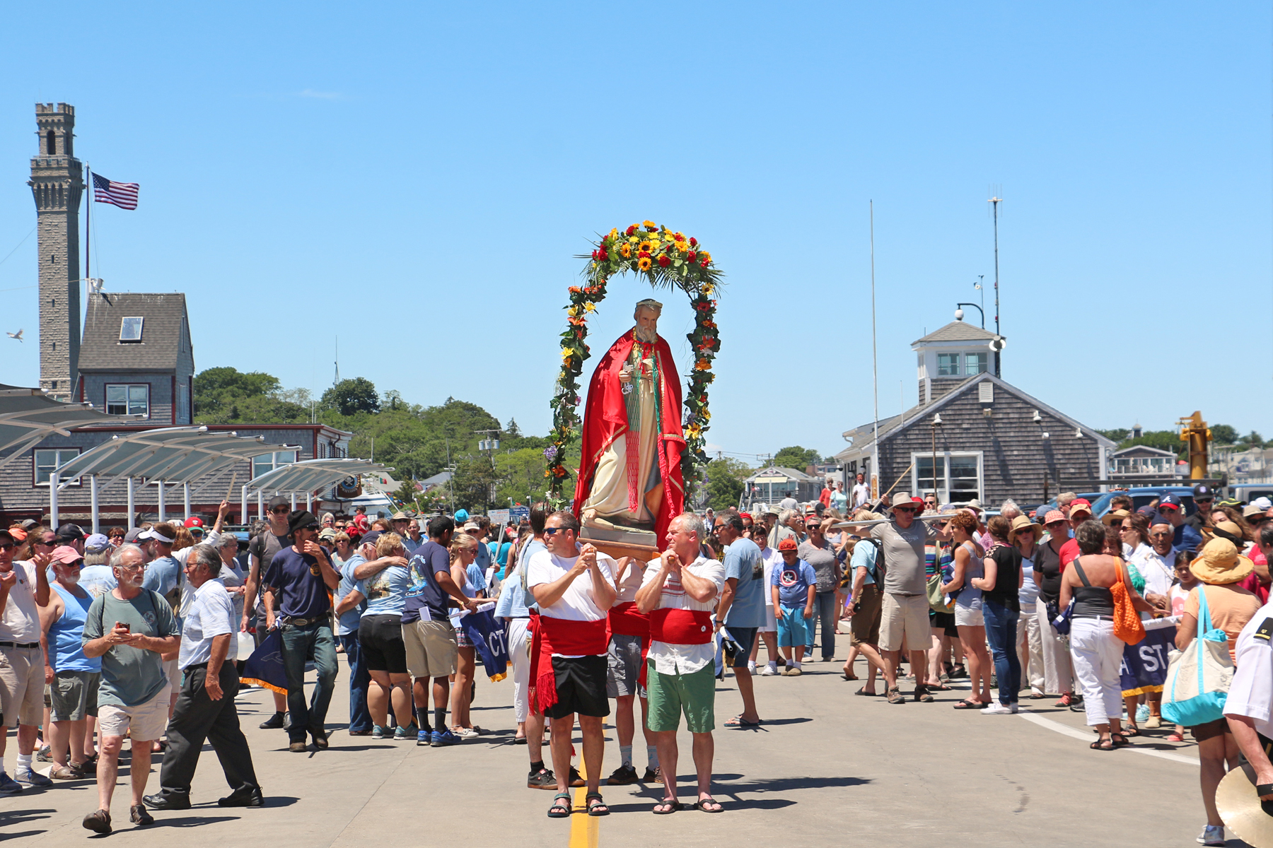 A statue of Saint Peter sporting the colors of the Portuguese flag is carried onto MacMillian Pier. In the background to the left stands the Pilgrim Monument, built in 1910 to commemorate the 1620 signing of the Mayflower Compact in Provincetown.