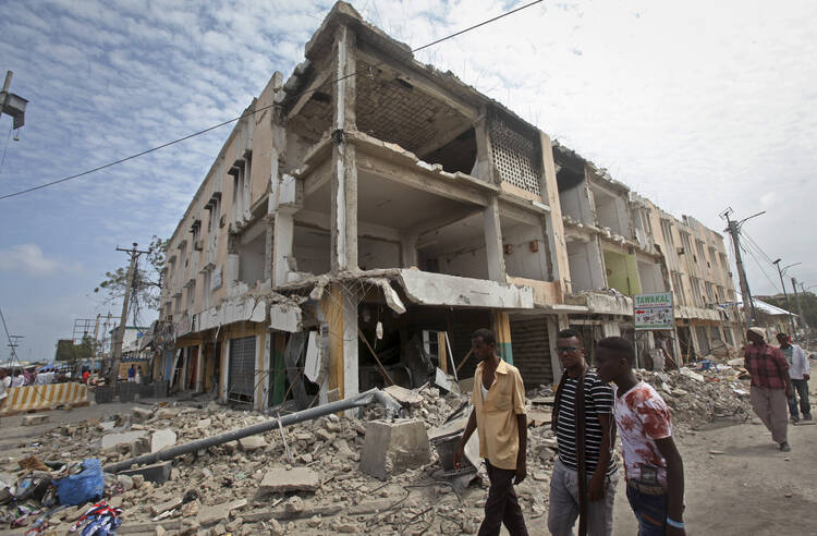 Men walk near destroyed buildings as thousands of Somalis gathered to pray at the site of the country's deadliest attack and to mourn hundreds of victims at the site of the attack in Mogadishu, Somalia, on Oct. 20. (AP Photo/Farah Abdi Warsameh)